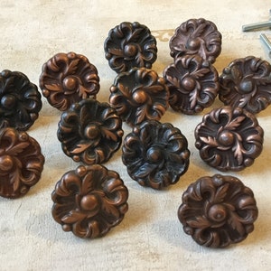 May include: A collection of 13 ornate, decorative cabinet knobs with a floral design. The knobs are made of metal and have a dark brown finish with copper accents.