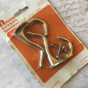 May include: A package of two gold-toned metal coat hooks with screws. The package is labeled "National Hardware Specialties" and "Crochet de garde-robe".