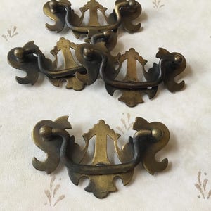 May include: Five antique brass drawer pulls with ornate designs. Each pull has a loop handle and decorative details.