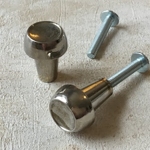 May include: Two silver cabinet knobs with screws. The knobs are round with a raised center and a smooth finish.