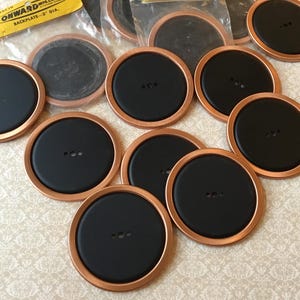 May include: A selection of black and copper-coloured circular items. Each has a black centre with three small holes and a copper-coloured rim. Some are packaged in clear plastic. A yellow label reads "ONWARD MFG. CO. BACKPLATE - 7.6 cm DIA."