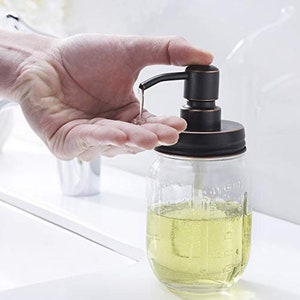 May include: A black and clear glass pump bottle with a black metal pump top and a clear glass jar with a black metal lid. The bottle is filled with a clear liquid.