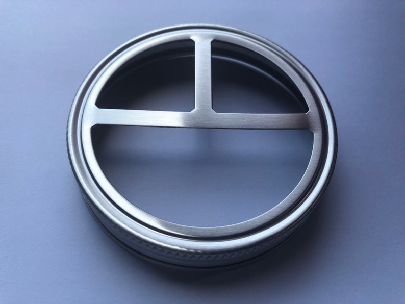 Puede incluir: Una tapa de metal plateada con una abertura de tres secciones para un frasco.