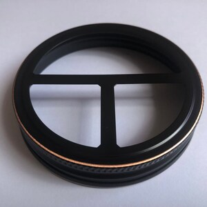 Puede incluir: Tapa de tarro de metal negro con borde dorado y dise&ntilde;o de tres puntas.