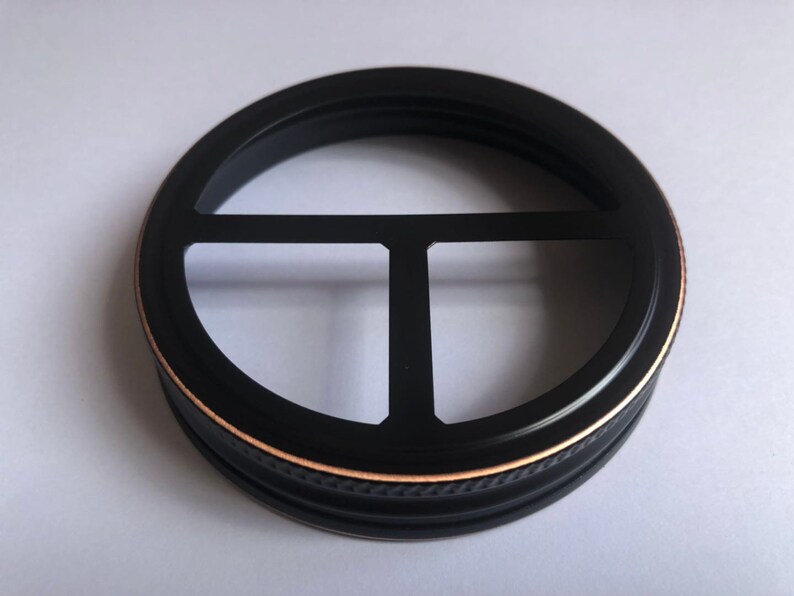 Puede incluir: Tapa de tarro de metal negro con borde dorado y dise&ntilde;o de tres puntas.
