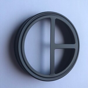 Puede incluir: Anillo de metal negro con un dise&ntilde;o circular que presenta tres recortes. El anillo tiene un acabado liso y pulido.