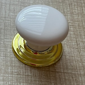 May include: White ceramic door knob with a gold metal base. The knob is round and has a smooth surface.