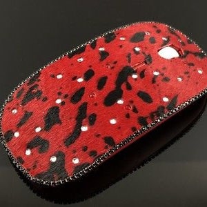 May include: A red and black computer mouse with a black trim and rhinestones. The mouse has a leopard print design.