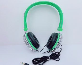 May include: Green headphones with black earcups and silver spikes. The headphones have a black cord.