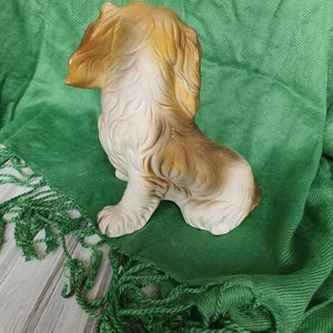 May include: A ceramic figurine of a brown and white dog sitting on a green fabric background.
