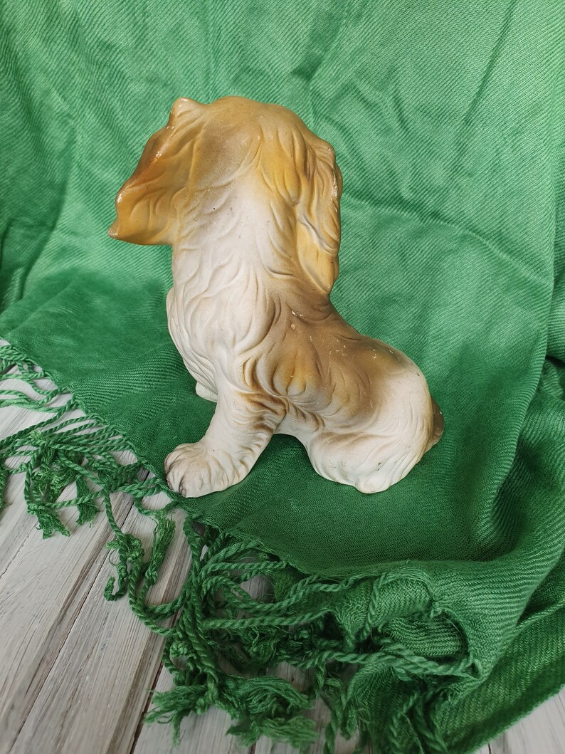 May include: A ceramic figurine of a brown and white dog sitting on a green fabric background.