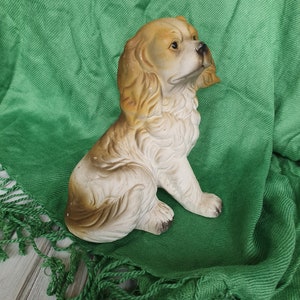 May include: A ceramic figurine of a brown and white dog with floppy ears. The dog is sitting on a green fabric background.