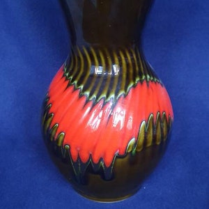 May include: A brown ceramic vase with a red and green glaze design. The vase has a wide mouth and a narrow base.