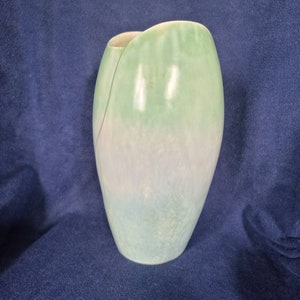 May include: A light green and blue ceramic vase with a unique, asymmetrical shape. The vase has a smooth, glossy finish and a subtle ombre effect.