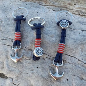 Puede incluir: Tres llaveros con paracord azul marino y rojo, cada uno con un dije de ancla y brújula de plata.