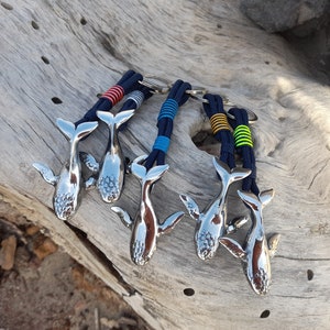 Può includere: Cinque portachiavi a forma di balena argentati con cordini a righe blu e bianche, blu e gialle e blu e verdi.