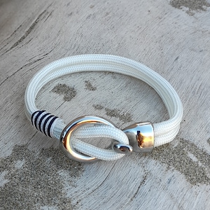 Puede incluir: Pulsera de cuerda blanca con cierre de gancho plateado y detalle de rayas azul marino.