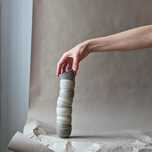 Könnte beinhalten: Ein Stapel kleiner, grauer und weißer Keramikbecher, die zu einem Turm gestapelt sind, mit einer Hand, die nach unten greift, um den oberen Becher zu nehmen.