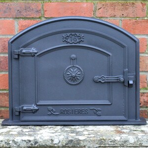 May include: Black cast iron oven door with a rounded top and a single door. The door has a decorative handle and a latch. The door is labelled "ROSIERES".