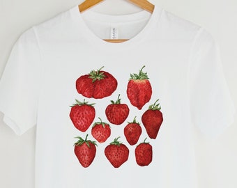 May include: White t-shirt with a red strawberry print. The strawberries are arranged in a cluster on the front of the shirt.