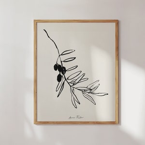 May include: Black and white line art print of an olive branch with olives. The print is framed in a natural wood frame and has the artist's signature "Anna Fisher" in the bottom right corner.