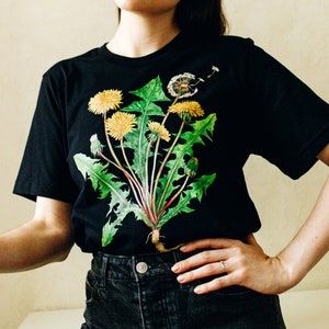 May include: Black t-shirt with a graphic print of dandelion flowers in shades of green and yellow.
