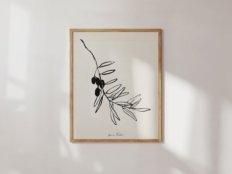May include: Black and white line art print of an olive branch with olives. The print is framed in a natural wood frame and has the artist's signature "Anna Fisher" in the bottom right corner.