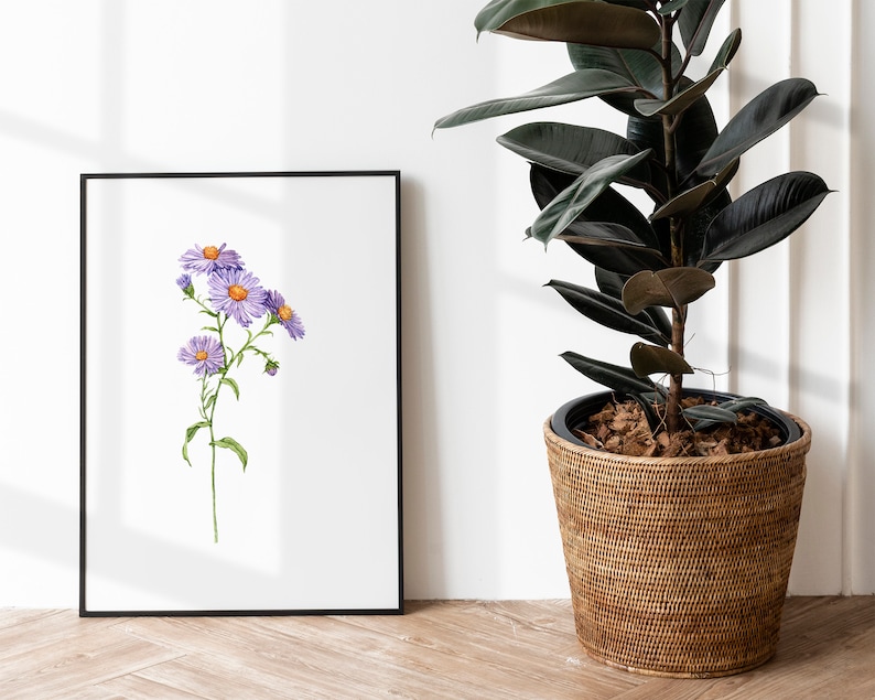May include: A framed watercolor painting of a purple flower with yellow centers. The painting is hanging on a white wall next to a potted plant.