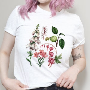 May include: White t-shirt with a floral print featuring pink, white, and green flowers. The flowers are illustrated in a watercolor style.