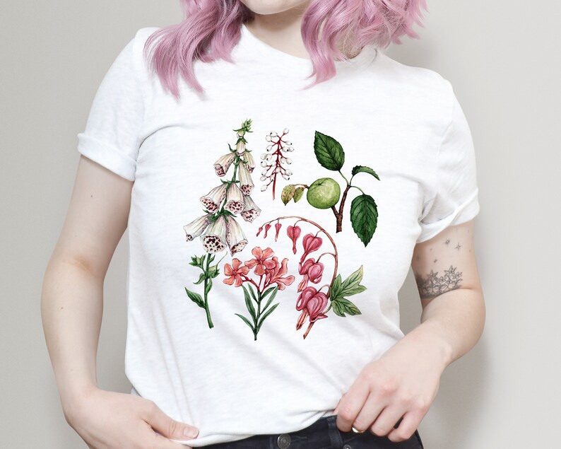 May include: White t-shirt with a floral print featuring pink, white, and green flowers. The flowers are illustrated in a watercolor style.