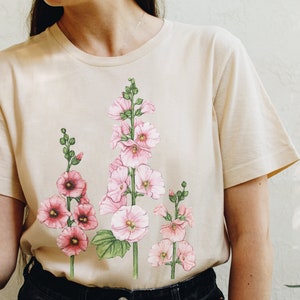May include: A beige t-shirt with a floral print of pink hollyhock flowers on the front.