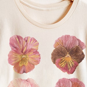 May include: A cream-colored t-shirt with a floral print of four pink and yellow pansies.