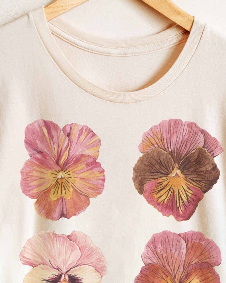 May include: A cream-colored t-shirt with a floral print of four pink and yellow pansies.