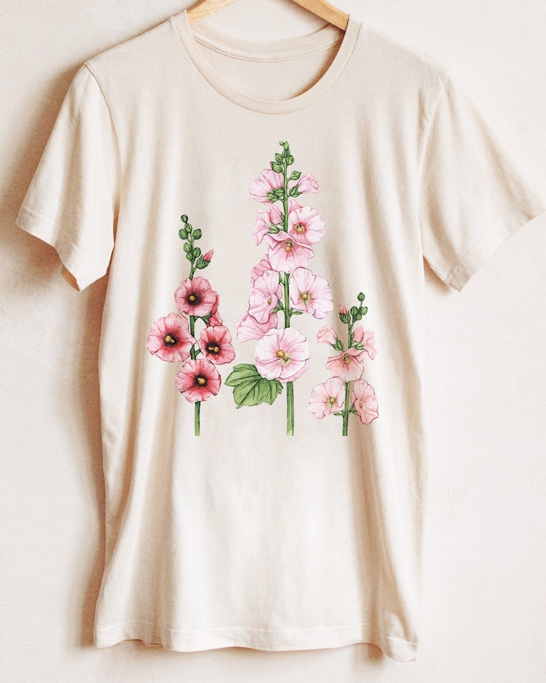 May include: A beige t-shirt with a floral print of pink and white hollyhocks.