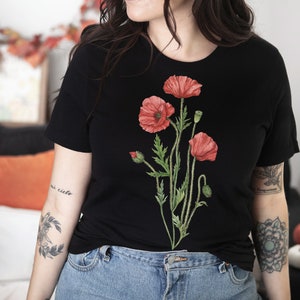 May include: A black t-shirt with a floral design featuring red poppies. The design is centered on the shirt and features green stems and leaves.