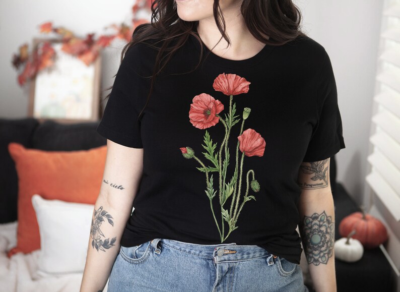 May include: A black t-shirt with a floral design featuring red poppies. The design is centered on the shirt and features green stems and leaves.