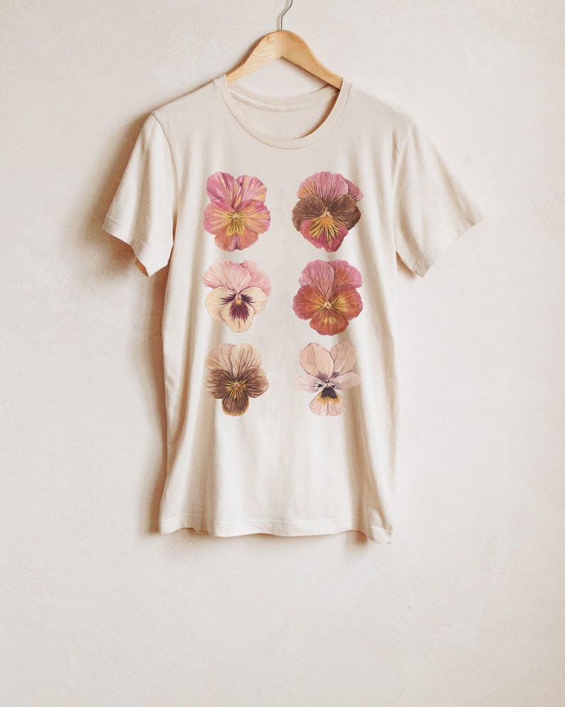 May include: A cream-colored t-shirt with a floral print of six pink and brown pansies.