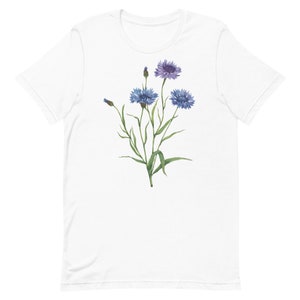 May include: White t-shirt with a watercolor illustration of blue and purple wildflowers with green stems and leaves.
