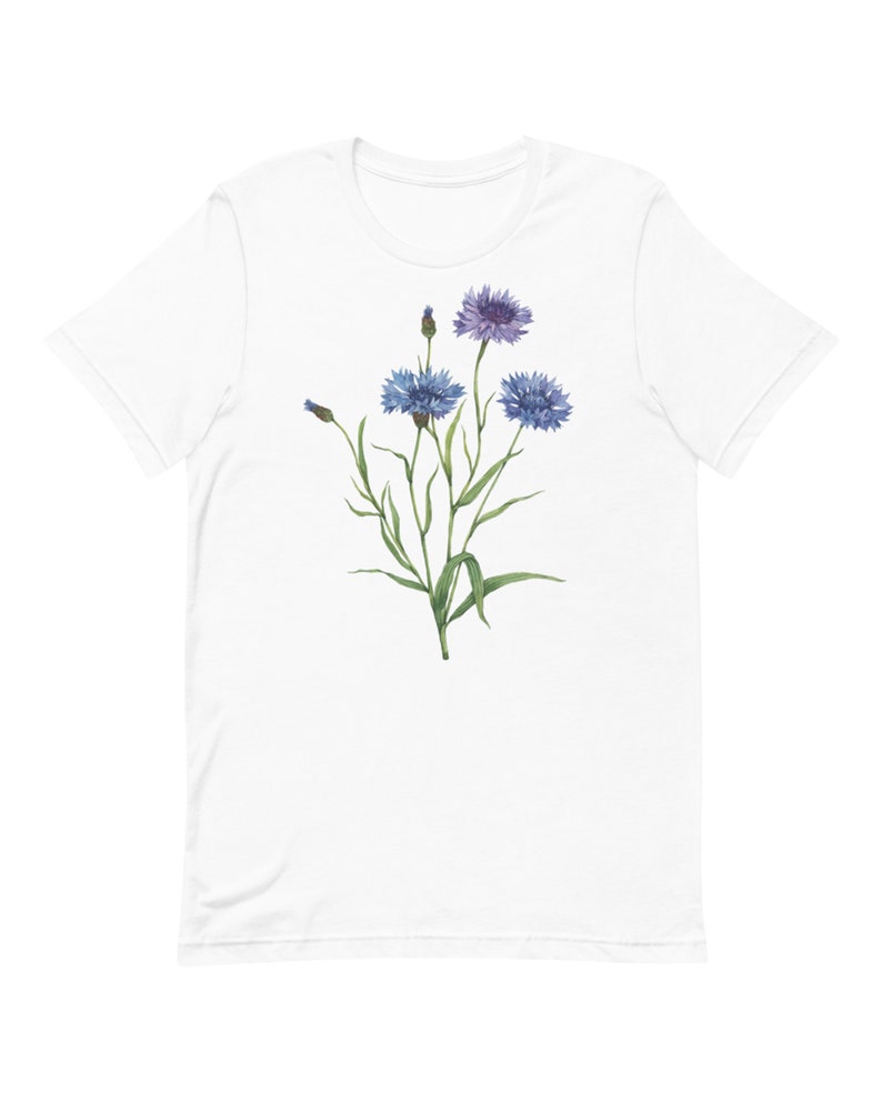 May include: White t-shirt with a watercolor illustration of blue and purple wildflowers with green stems and leaves.