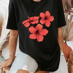Może przedstawiać: Czarny, oversize'owy t-shirt z nadrukiem graficznym trzech czerwonych kwiat&oacute;w hibiskusa.