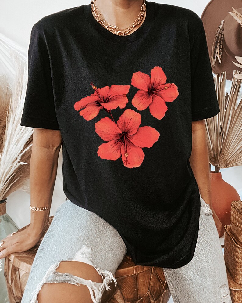 Może przedstawiać: Czarny, oversize'owy t-shirt z nadrukiem graficznym trzech czerwonych kwiat&oacute;w hibiskusa.