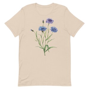 May include: A beige t-shirt with a floral design featuring blue and purple wildflowers with green stems and leaves.