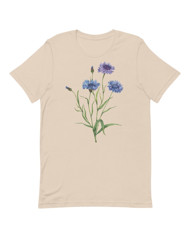 May include: A beige t-shirt with a floral design featuring blue and purple wildflowers with green stems and leaves.