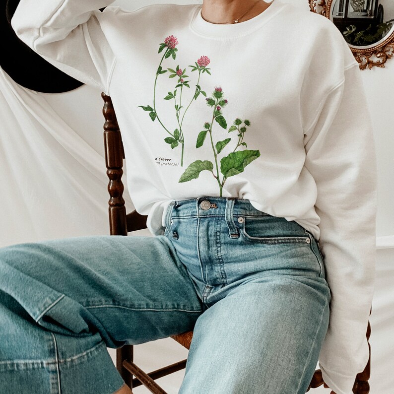 May include: A white sweatshirt with a botanical illustration of clover flowers and leaves. The text "4 Clover" and "Trifolium repens" is printed below the illustration.