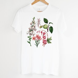 May include: White t-shirt with a floral print featuring pink, white, and green flowers. The flowers are illustrated in a watercolor style.