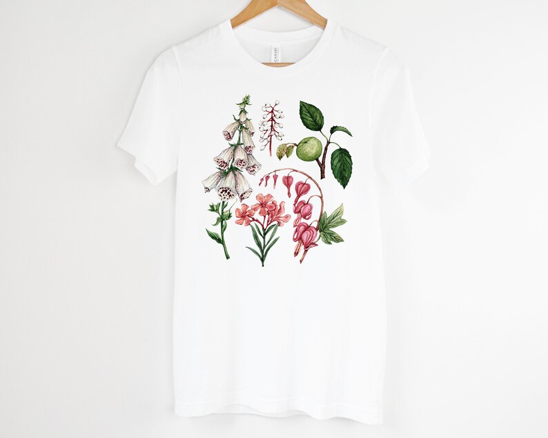 May include: White t-shirt with a floral print featuring pink, white, and green flowers. The flowers are illustrated in a watercolor style.
