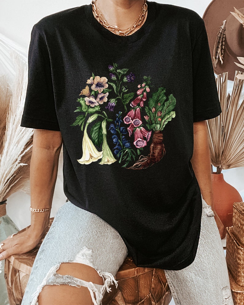May include: Black oversized t-shirt with a floral print featuring a variety of flowers in shades of pink, purple, white, and green. The flowers are arranged in a circular pattern and have a vintage botanical illustration style.