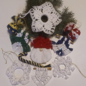 Op de afbeelding: Een verzameling handgemaakte kerstversieringen met verschillende ontwerpen, waaronder sneeuwvlokken, een kabouter en een snoepstok. De versieringen zijn gemaakt van wit garen en hebben kleurrijke accenten.