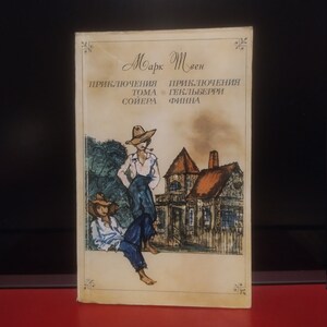 Op de afbeelding: Een vintage boekomslag met een aquarel-illustratie van twee mensen die voor een huis staan. De titel van het boek is "De avonturen van Tom Sawyer" door Mark Twain.