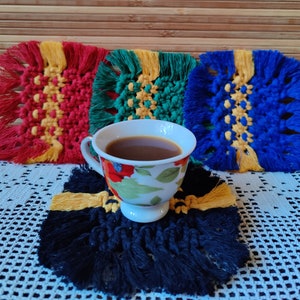 Könnte beinhalten: Eine Tasse Kaffee oder Tee steht auf einem gehäkelten Untersetzer in Schwarz und Gelb. Der Untersetzer ist von drei weiteren gehäkelten Untersetzern in Rot, Grün und Blau umgeben.